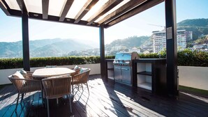 An outdoor patio with a wooden deck, a round table with chairs, and a built-in grill.