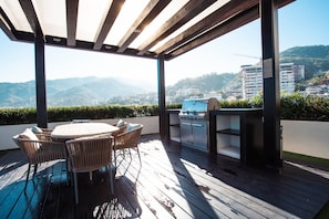 Une terrasse extérieure avec une table et des chaises, un barbecue et une vue sur un paysage montagneux.
