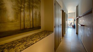 A hallway with a large abstract painting on the left, a marble bench, and a view into a room with a desk and chair.