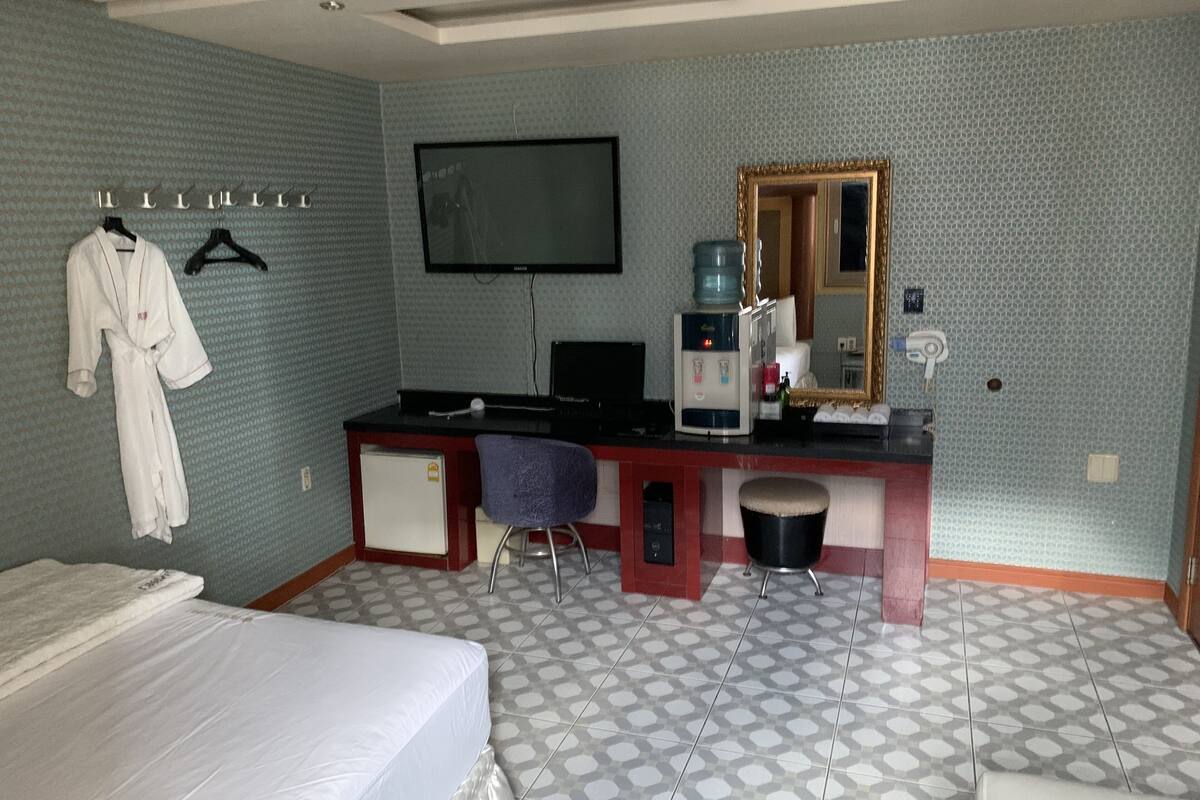 Une chambre d’hôtel équipée d’un lit, d’un bureau avec un ordinateur, d’une chaise, d’une machine à café, d’une télévision et d’un miroir.
