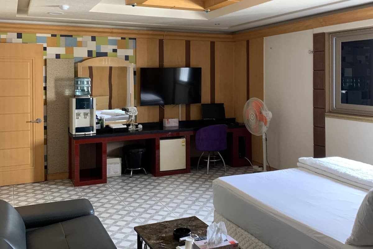 Une chambre d’hôtel comprenant un lit, un bureau avec une télévision, un canapé, un petit réfrigérateur et un distributeur d’eau.