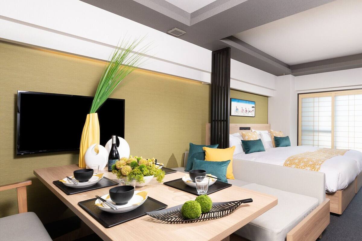 A hotel room with a bed, a dining table set for two, a TV, and a large window.