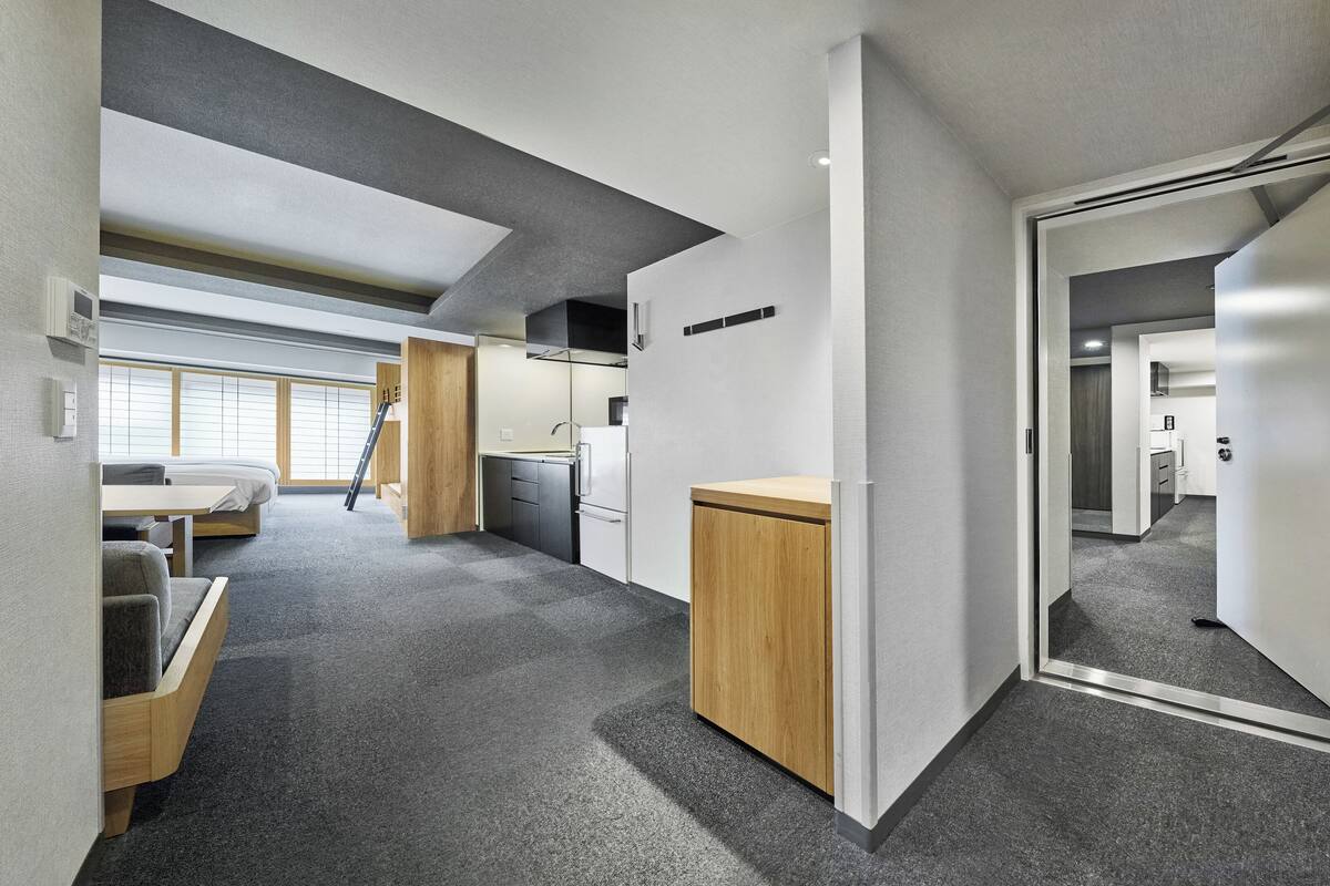 Moderni ja kompakti hotellihuone, jossa on pieni keittiönurkkaus, pieni oleskelualue ja suuri peili.