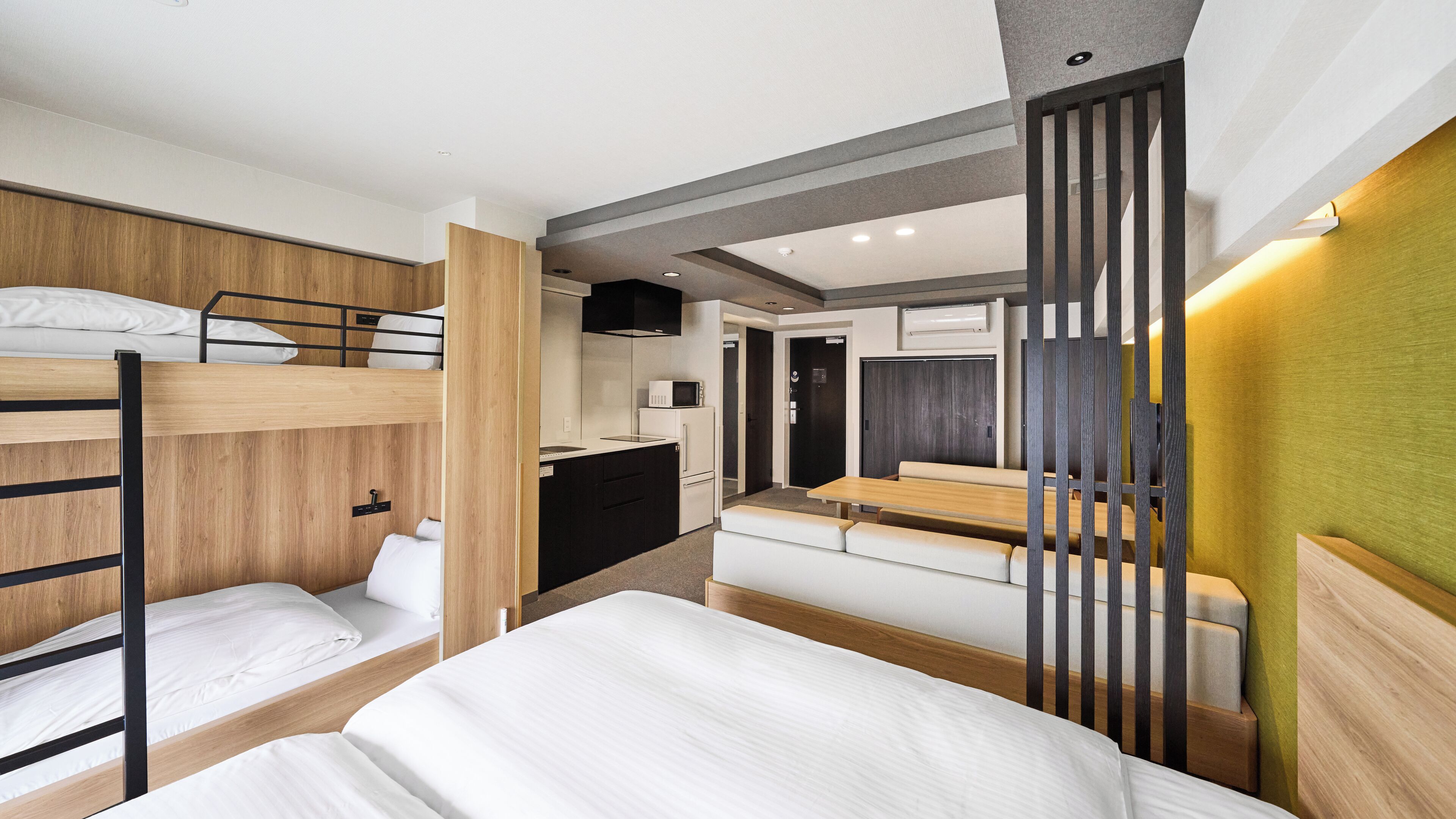 A compact hotel room with bunk beds, a kitchenette, and a seating area.