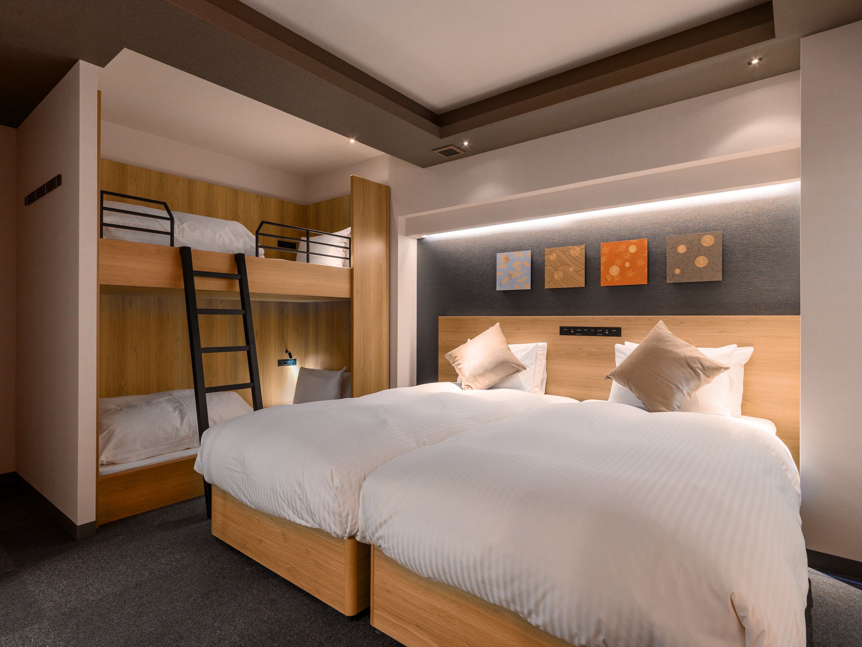 A modern hotel room with a bunk bed, a separate bed, and a headboard with built-in lighting.