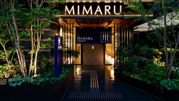 L'entrée de l'hôtel Mimaru Apartment, situé près de la gare de Kyoto, présente un design moderne avec un chemin menant à l'entrée, le tout étant agrémenté de verdure.