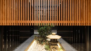 Un bâtiment moderne doté d’un plafond à lattes de bois, d’un jardin central agrémenté d’une lanterne en pierre et d’un sol carrelé.
