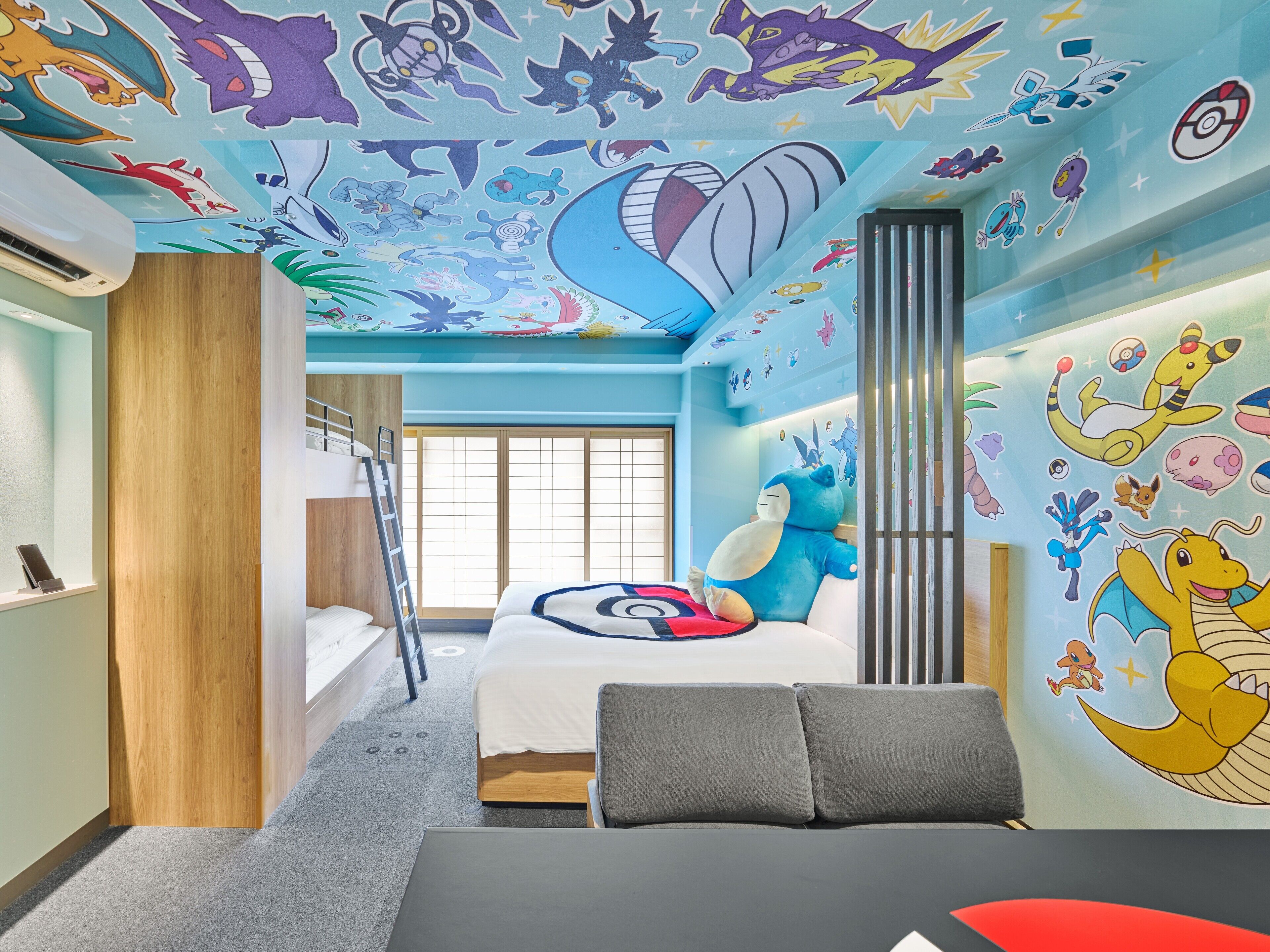 Une chambre avec un lit superposé, un bureau et une grande fresque murale représentant des personnages de Pokémon.
