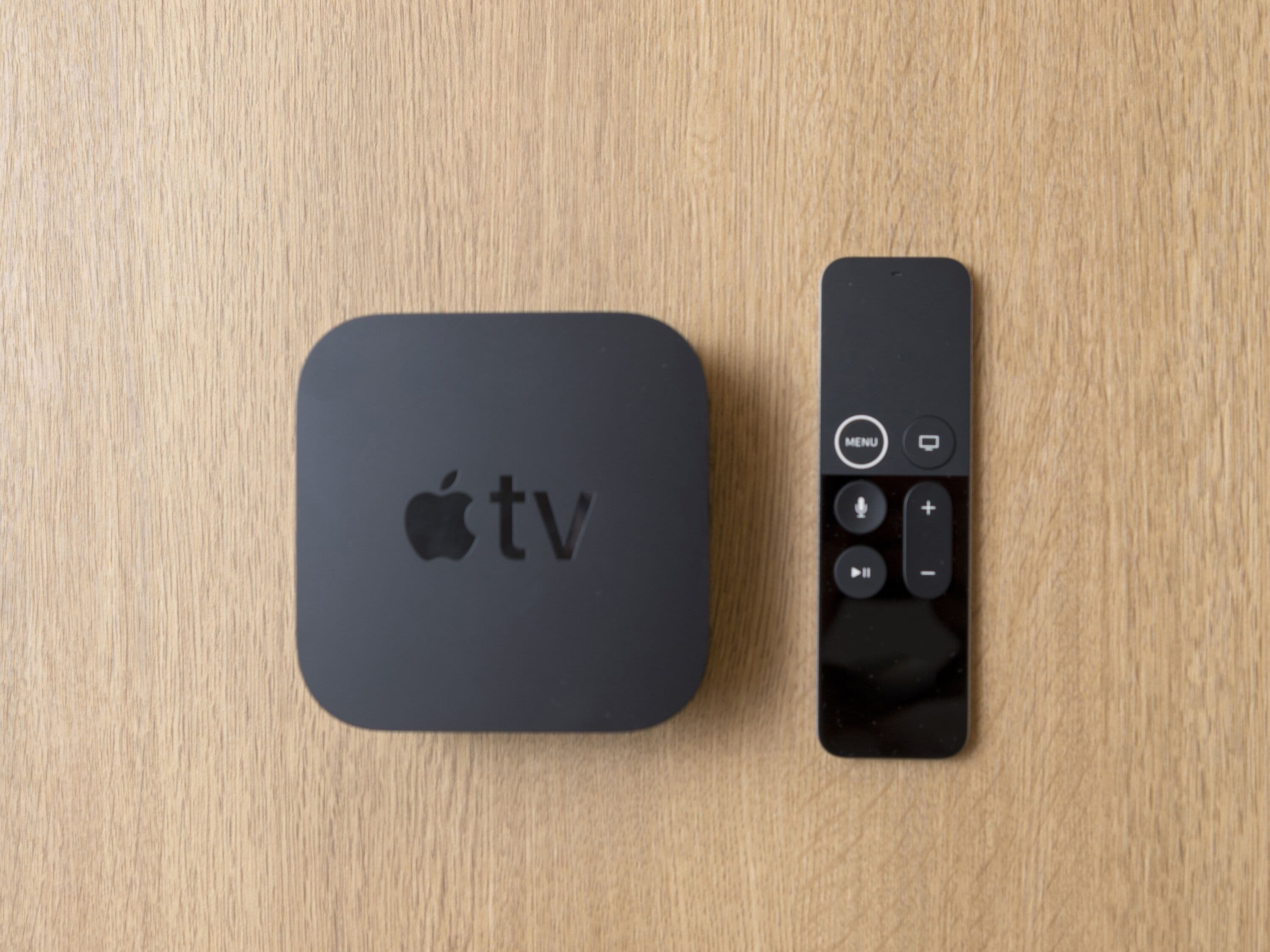 A black Apple TV box and remote on a wooden surface.