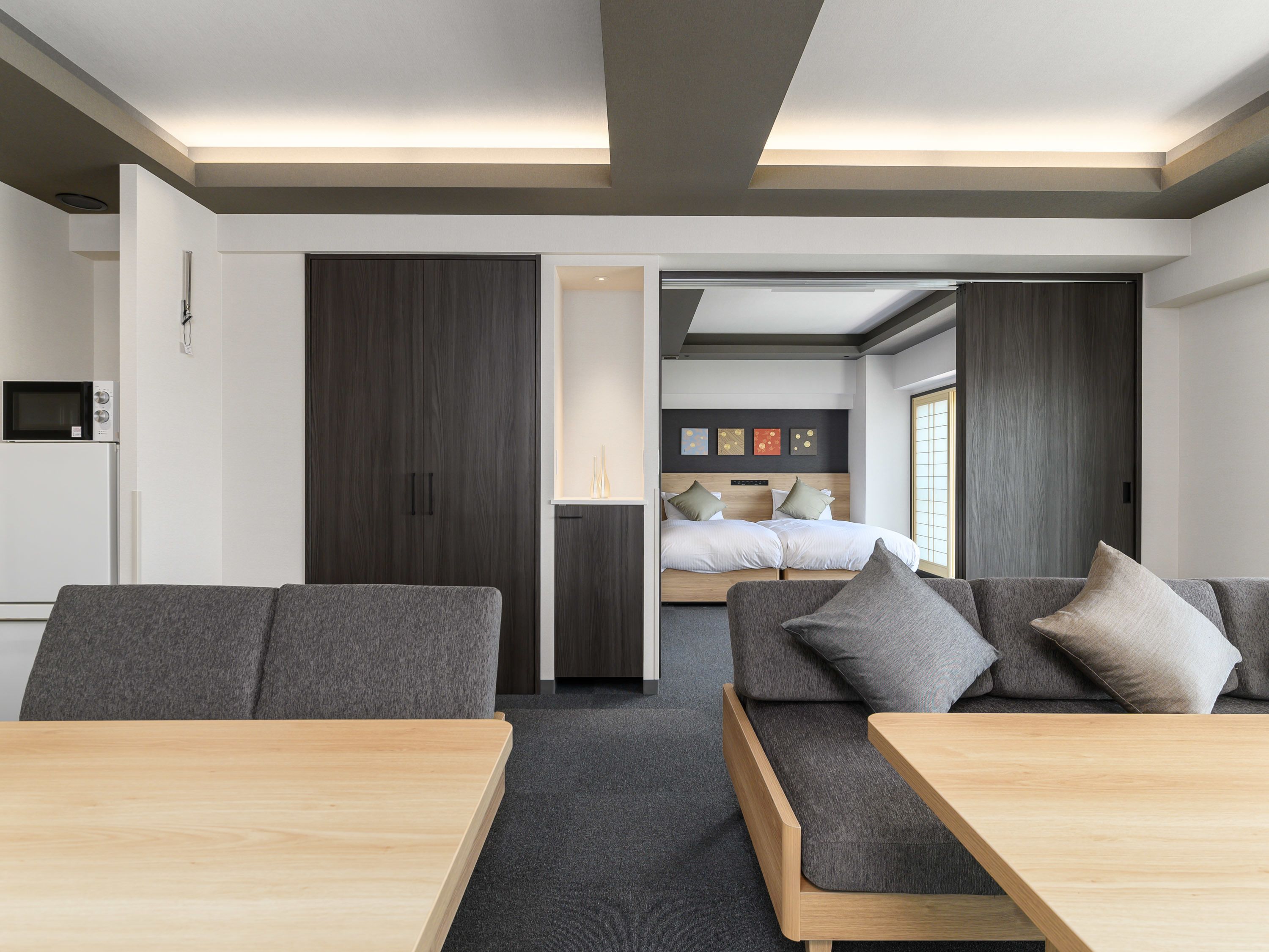 A modern hotel room with a sofa, a wooden table, a bed with a headboard, and a wardrobe.