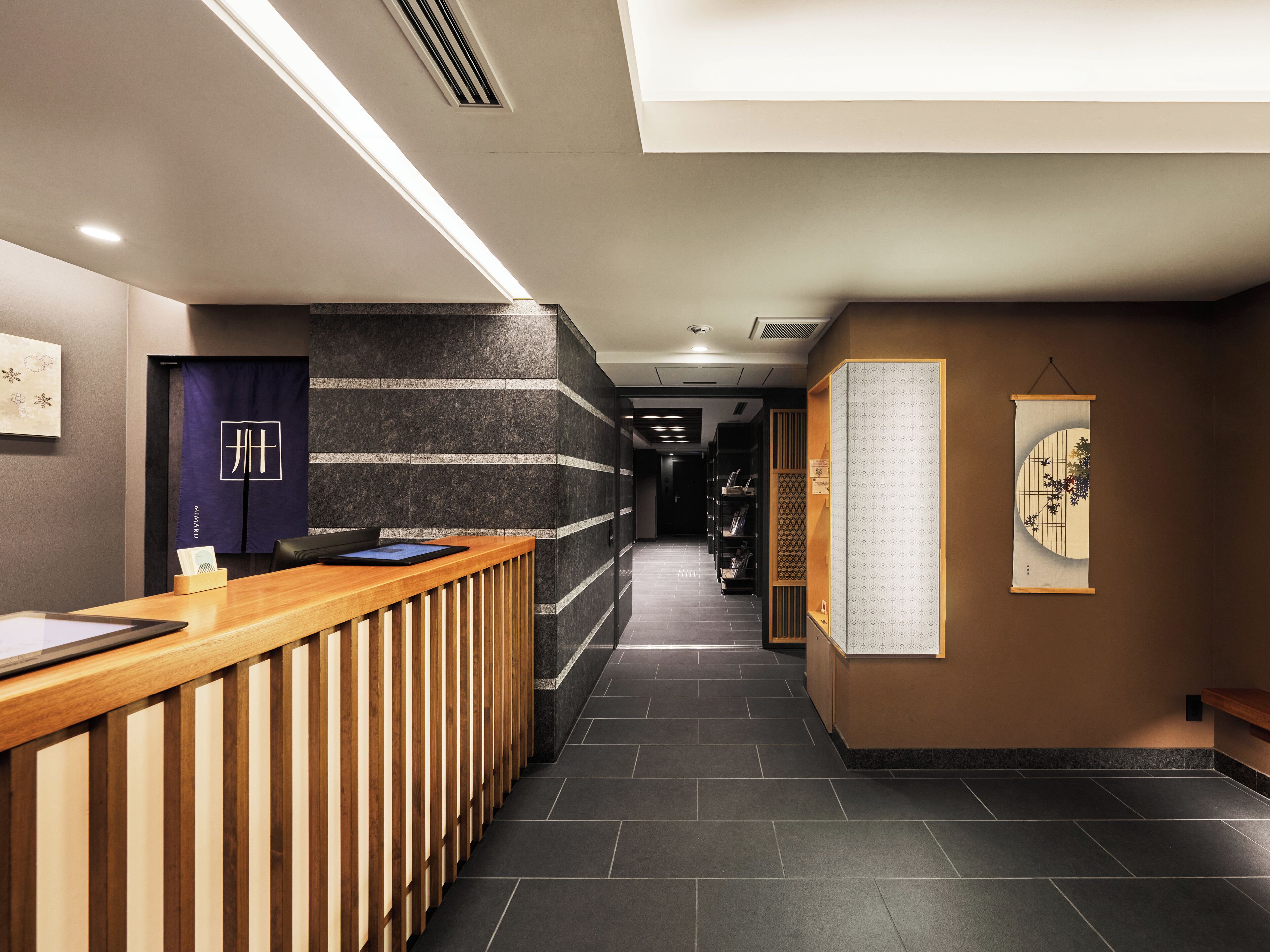 A reception area with a wooden reception desk, a dark wall with horizontal stripes, and a bulletin board with a framed picture.