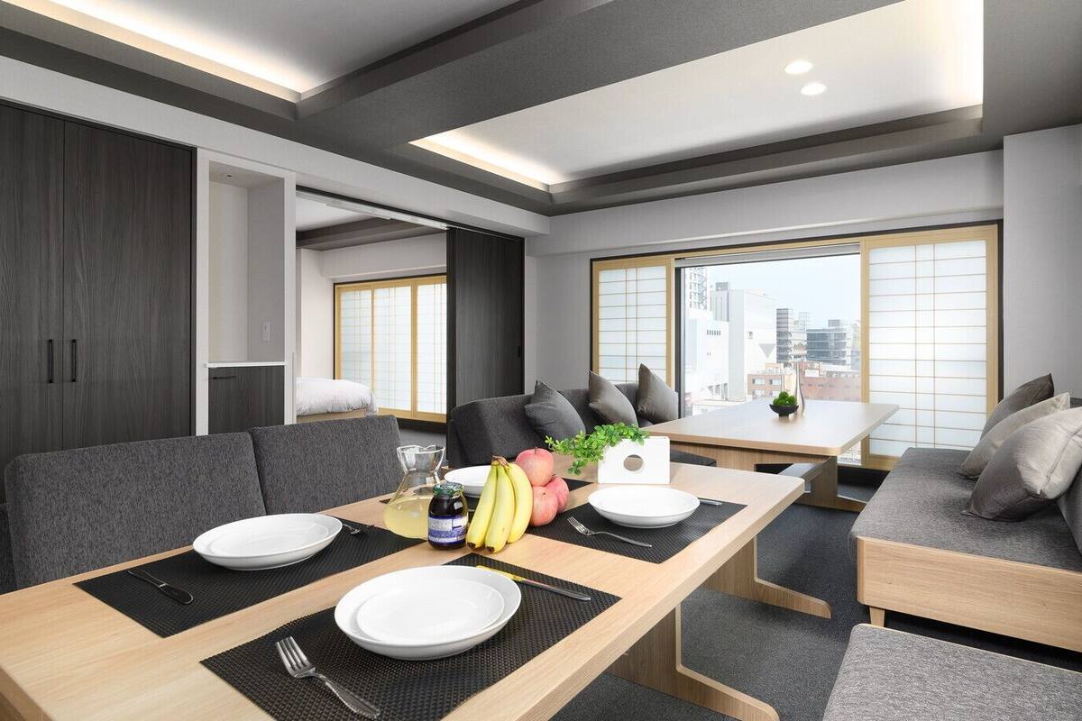A modern dining area with a wooden table, grey sofas, and a view of the city.