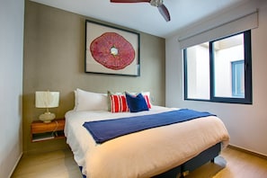 A bedroom with a bed, pillows, a nightstand, a lamp, a ceiling fan, and a large window.