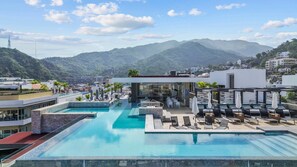 A rooftop infinity pool with lounge chairs and a bar area, overlooking a mountainous landscape.