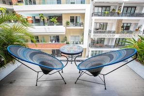 A balcony with two blue wicker chairs and a small round table.