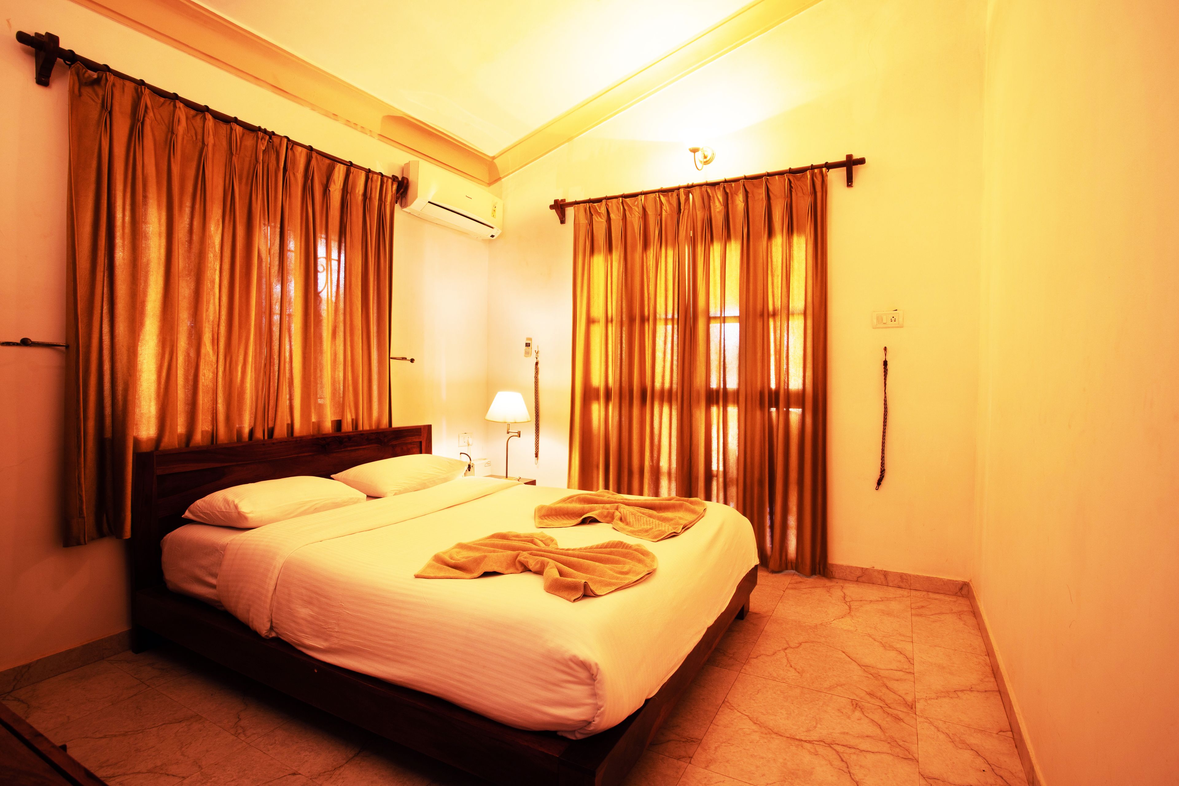 A hotel room with a large bed, curtains, a nightstand, and a lamp.
