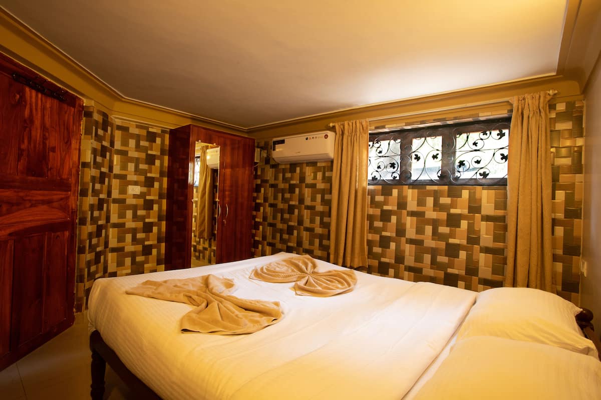 A hotel room with a bed, wooden wardrobe, air conditioning unit, patterned curtains, and a window with decorative ironwork.
