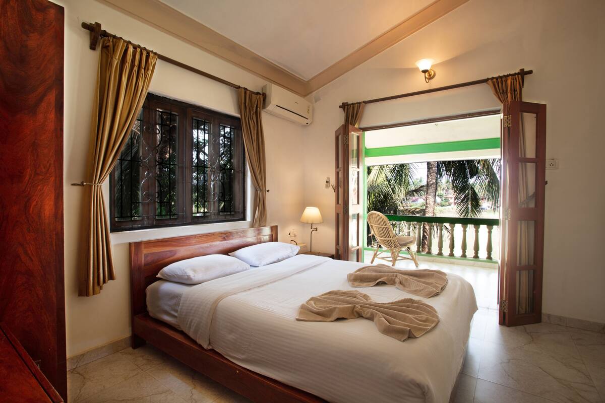 A hotel room with a bed, curtains, a window, a chair, and an air conditioning unit.