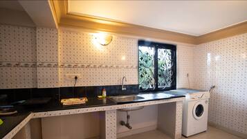 A kitchen with a sink, washing machine, and a window with decorative ironwork.