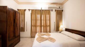 A hotel room with a wooden wardrobe, a bed with white linens, and a curtain rod with beige curtains.