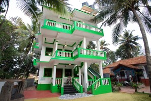 A multi-story building with green and white exterior walls, a staircase, and a small garden area with palm trees. - Casa Margarida (Calangute)