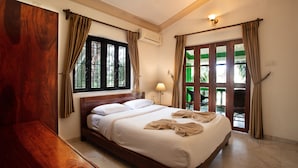 Un dormitorio espacioso con una cama grande, cabecera de madera y vistas a la vegetación por la ventana.