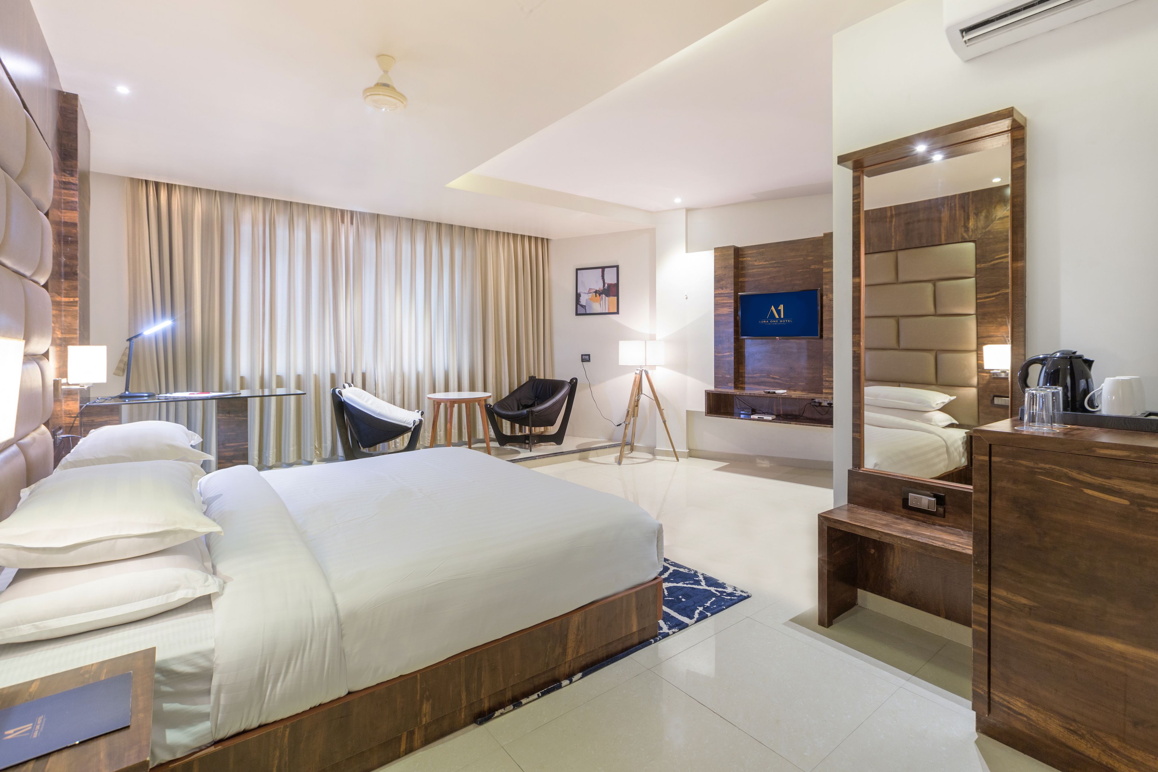 A modern hotel room with a large bed, a desk, a chair, a mirror, and a TV.