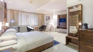 A modern hotel room with a large bed, a desk, a chair, a mirror, and a TV.