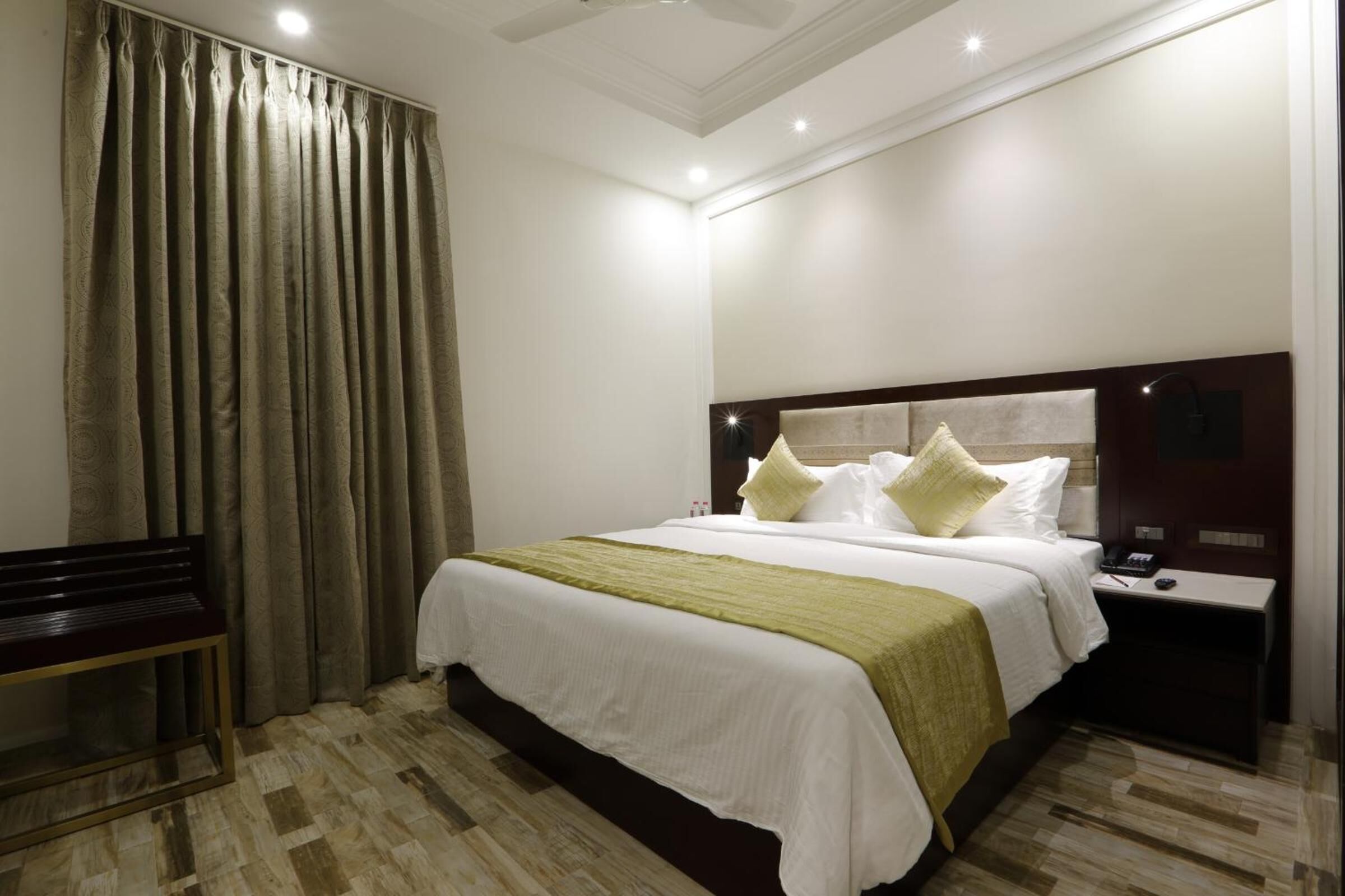 A hotel room with a large bed, a bedside table, a bench, and a curtain.
