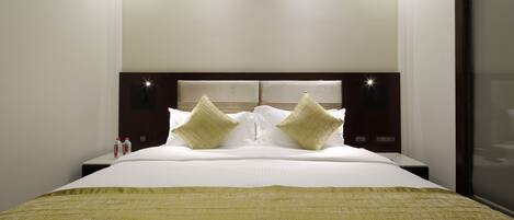 A neatly made bed with a white comforter and two pillows, a bedside table with a bottle, and a headboard with built-in lighting.