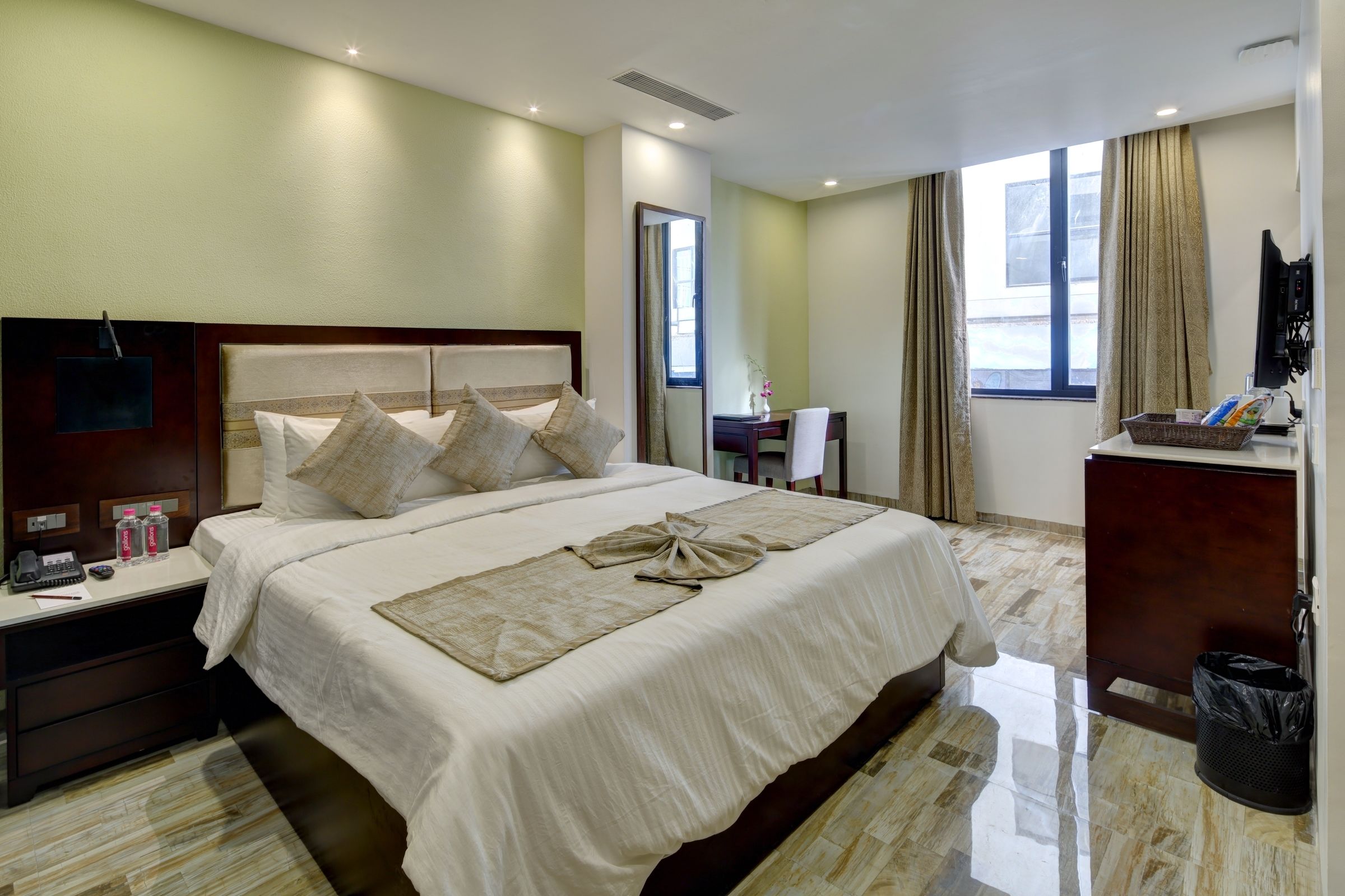 A hotel room with a large bed, a desk, a chair, a TV, and a trash bin.