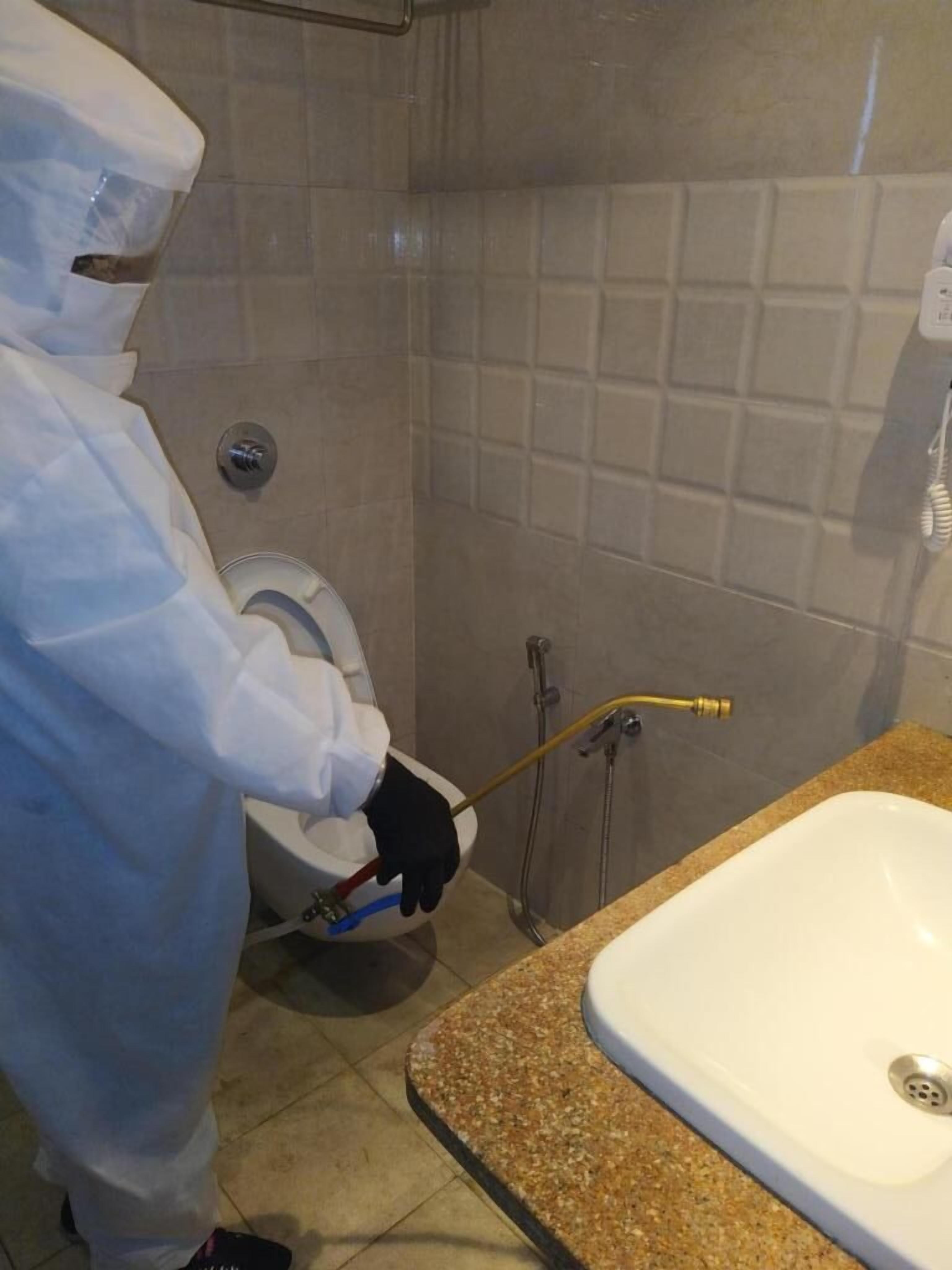 A person in a white protective suit cleaning a bathroom sink and toilet.
