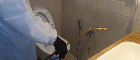 A person in a white protective suit cleaning a bathroom sink and toilet.