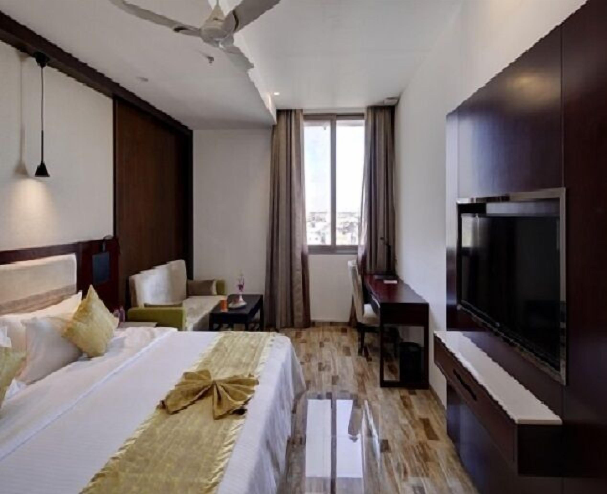 A hotel room with a bed, a desk, a chair, a TV, and a window with curtains.