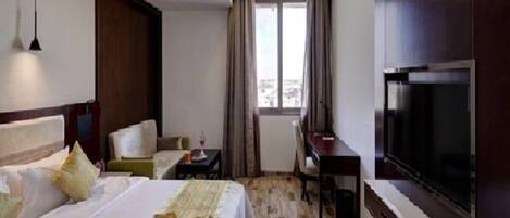 A hotel room with a bed, a desk, a chair, a TV, and a window with curtains.