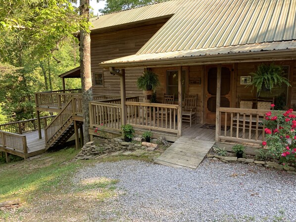 A rustic log cabin with a porch, wooden deck, and stone steps leading to the entrance.
