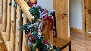 A wooden staircase with a garland of evergreen branches, pine cones, and red berries.
