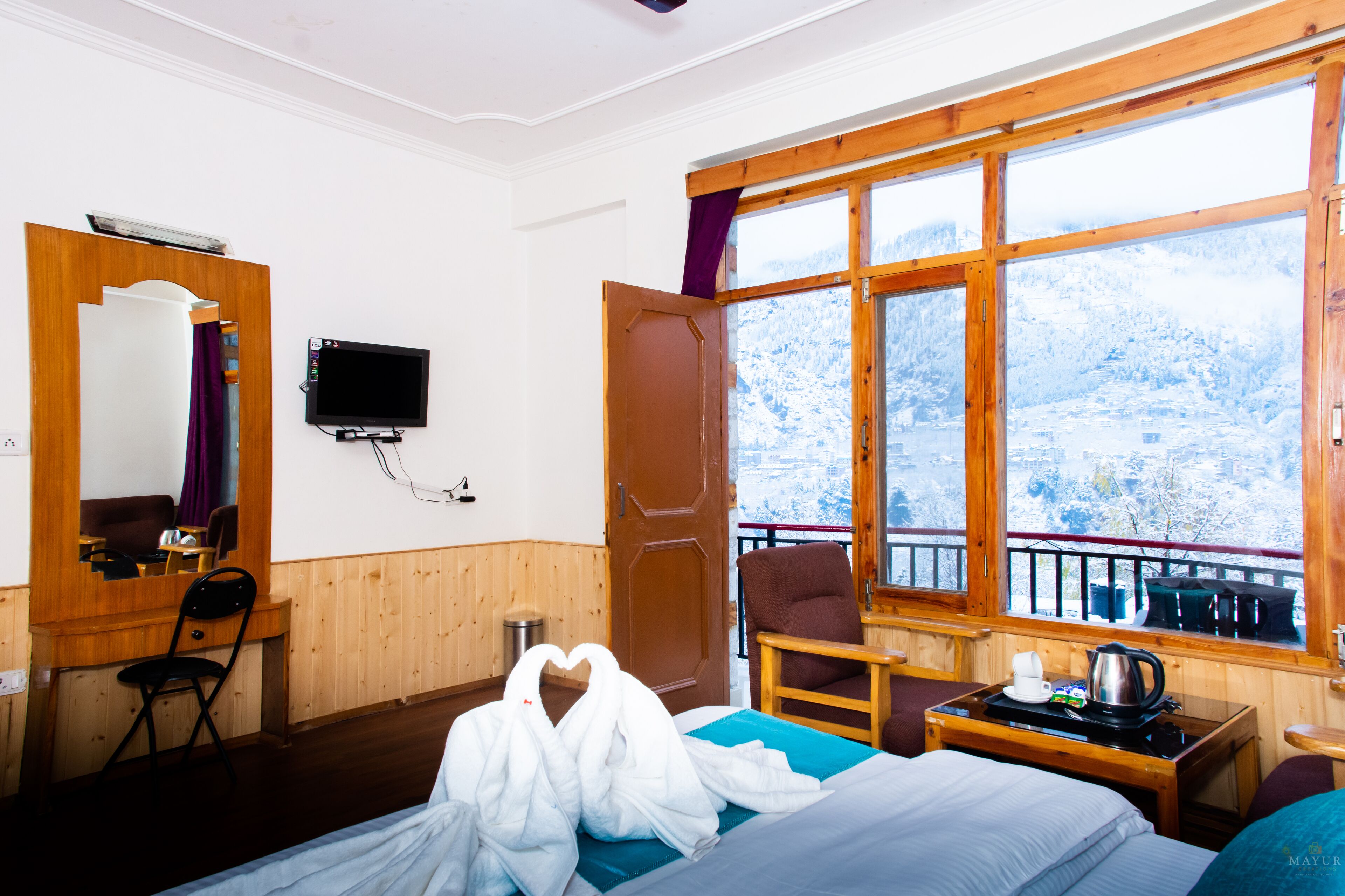 A hotel room with a bed, a desk with a chair, a television, and a window with a view of snow-covered mountains.