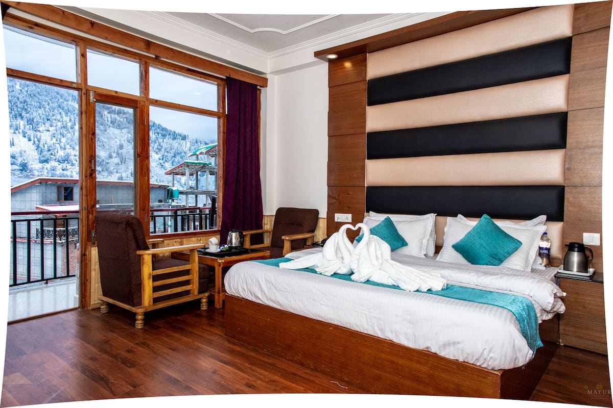 Habitación de hotel con una cama grande, cabecera de madera, un escritorio con silla y vistas a una montaña nevada.