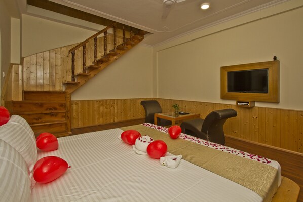 A hotel room with a wooden staircase, a bed with red balloons, a TV mounted on the wall, and a small table with a plant.