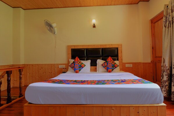 Un dormitorio con cabecera de madera, cama con colcha colorida, mesita de noche y ventilador de pared.