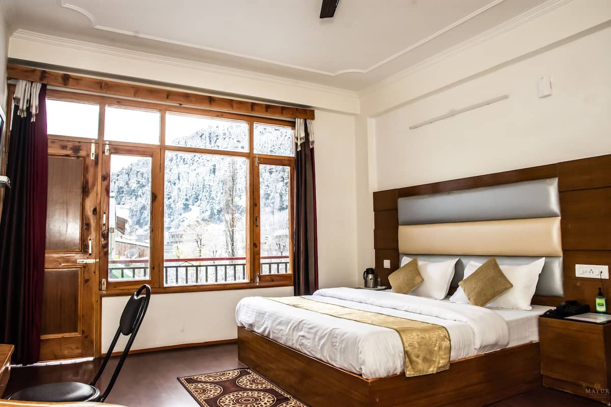 Un dormitorio con cama de madera, mesita de noche, silla y ventana con vista a árboles nevados.