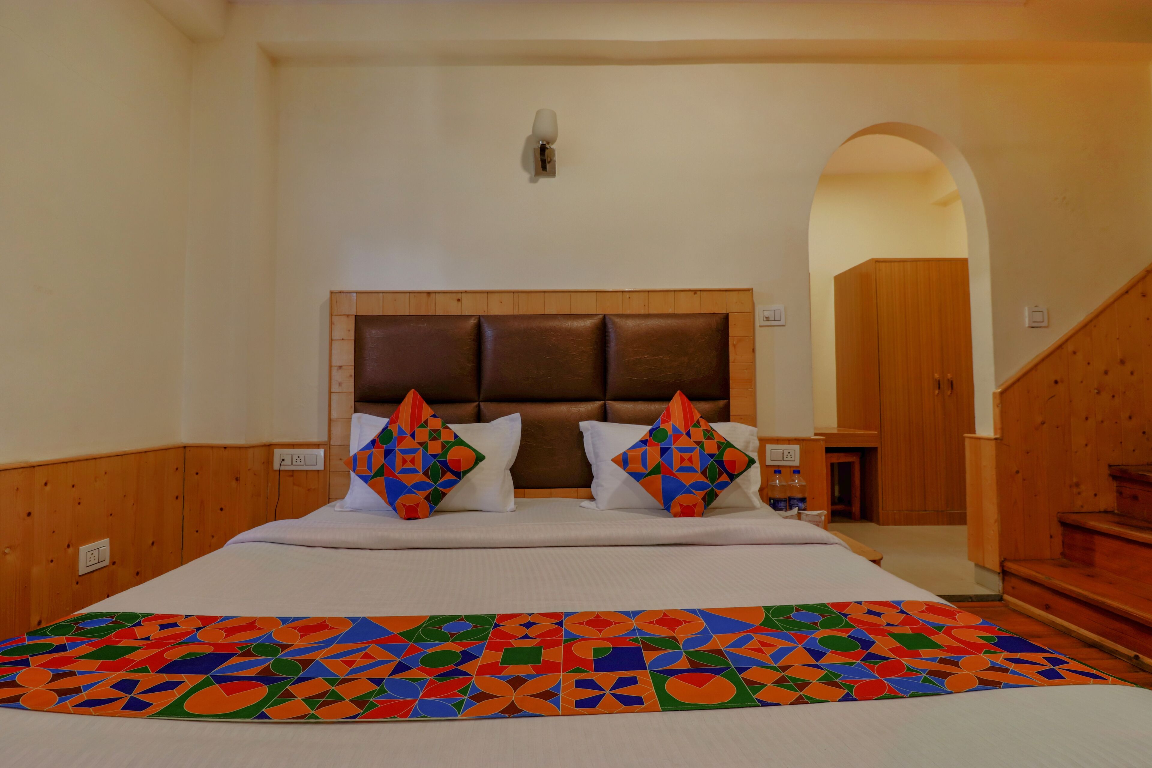 Een slaapkamer met een groot bed, een houten hoofdbord en een kleurrijke deken met een geometrisch patroon.