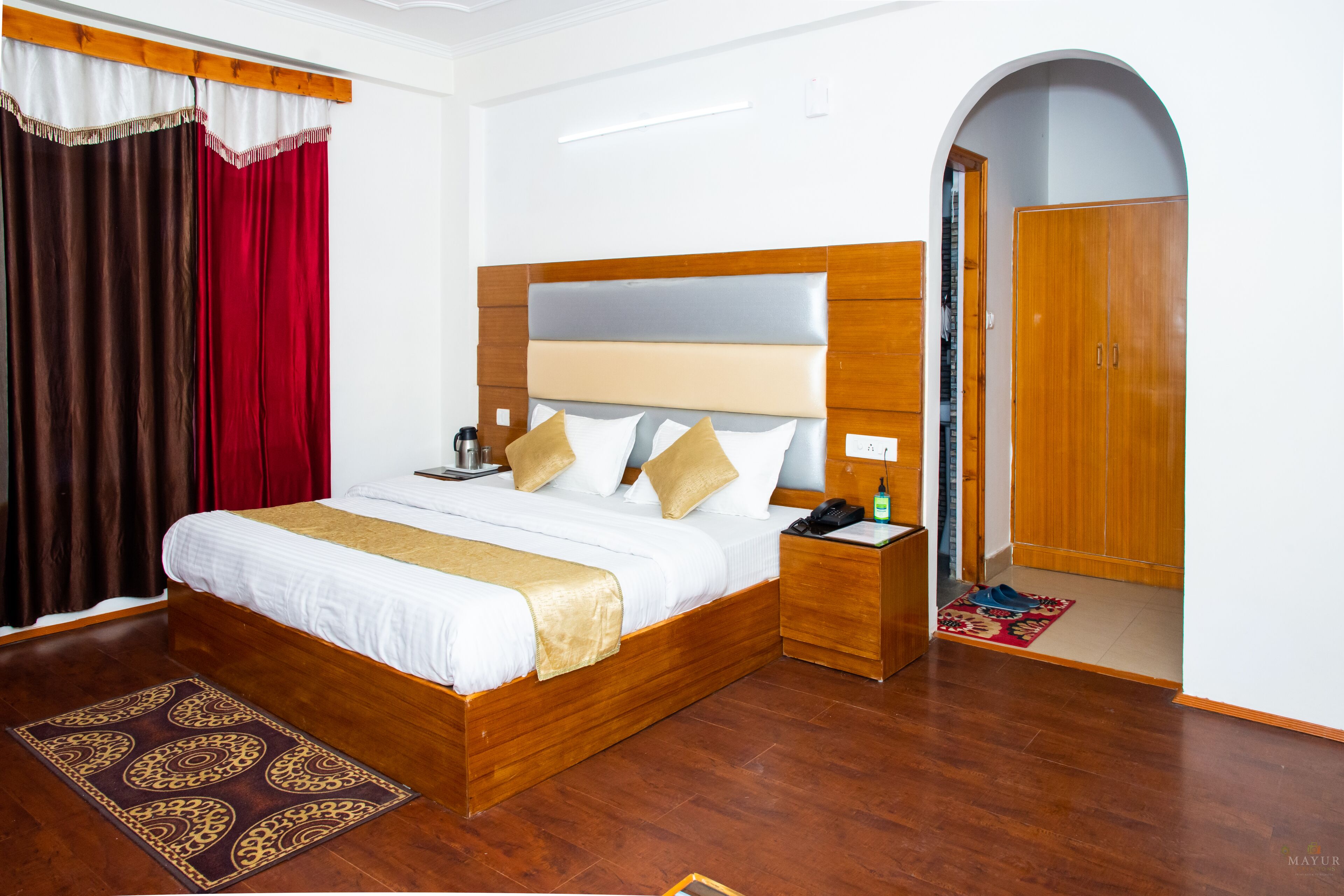 A neatly arranged hotel room with a wooden bed, a bedside table with a lamp, a nightstand, and a wardrobe.