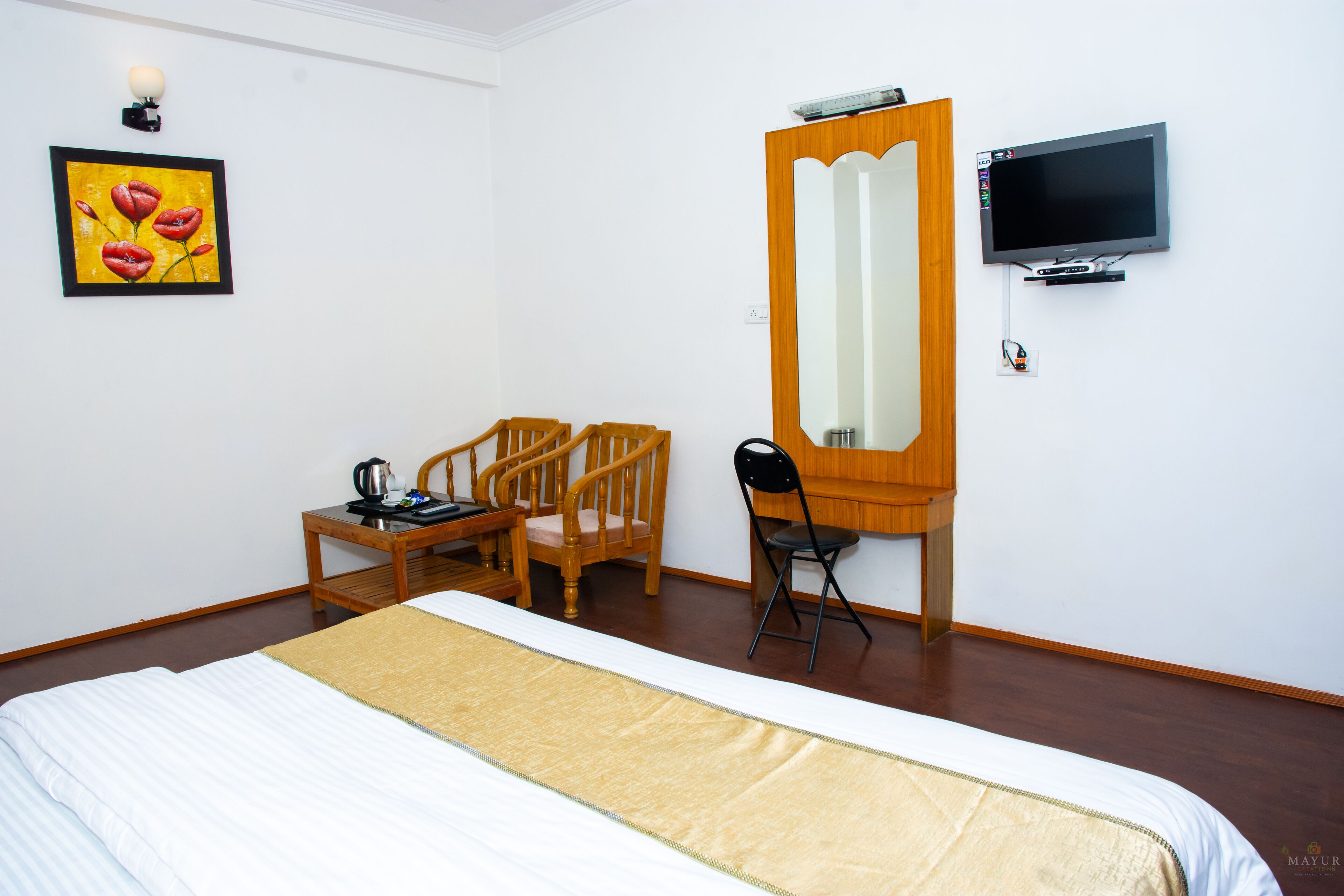 Una camera d'albergo con un letto, una scrivania con due sedie, una televisione e uno specchio fissato al muro.