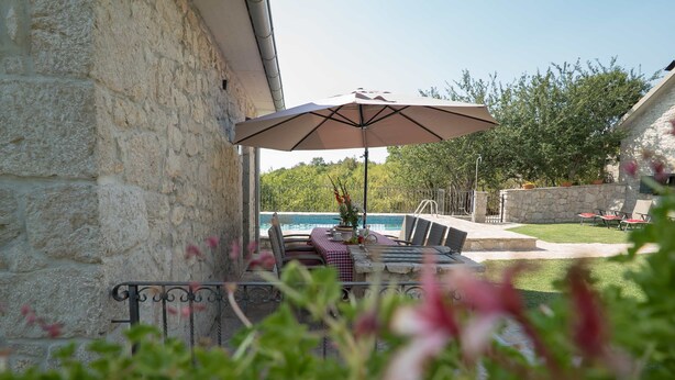Un bâtiment en pierre doté d’un patio comprenant un espace extérieur avec des sièges, une table recouverte d’une nappe à carreaux et un grand parasol.