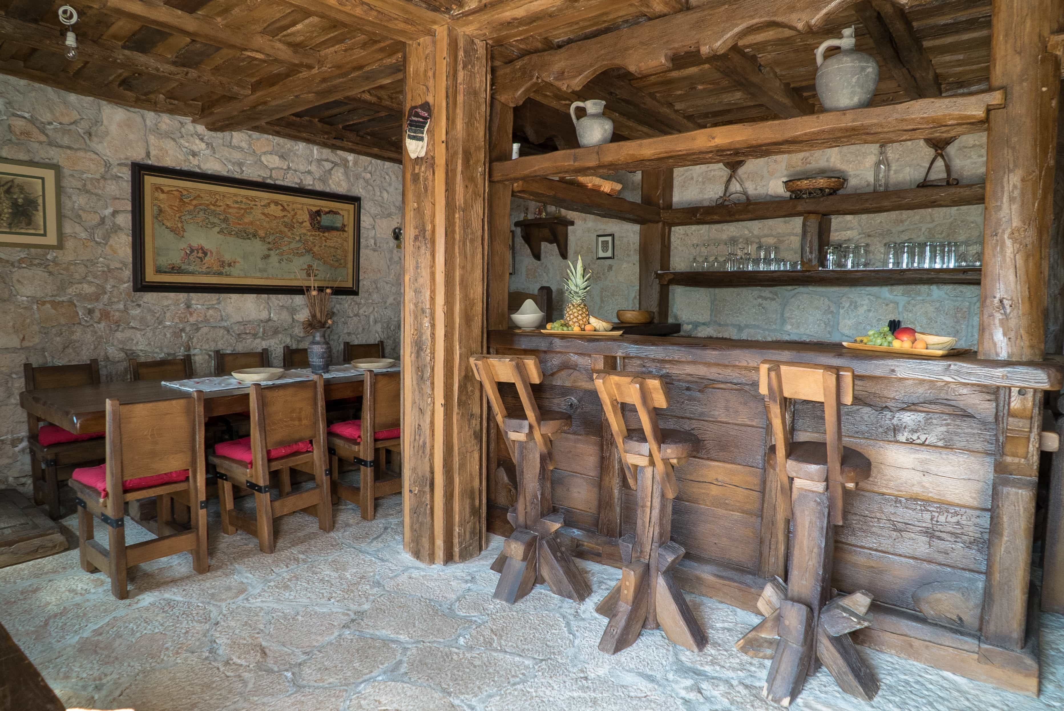 A rustic wooden interior with stone walls, a wooden bar area, and a dining setup with wooden chairs and tables.