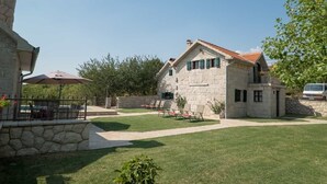 Un bâtiment en pierre avec un toit en tuiles, des places assises à l’extérieur et une pelouse bien entretenue.