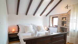 Une chambre à coucher avec un lit en bois, du linge de lit blanc, une cheminée en pierre et une table de chevet avec une lampe.