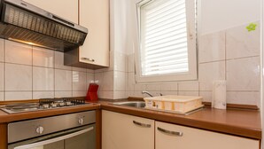 Une cuisine équipée d’une cuisinière, d’un four, d’un évier et d’une fenêtre avec des stores.